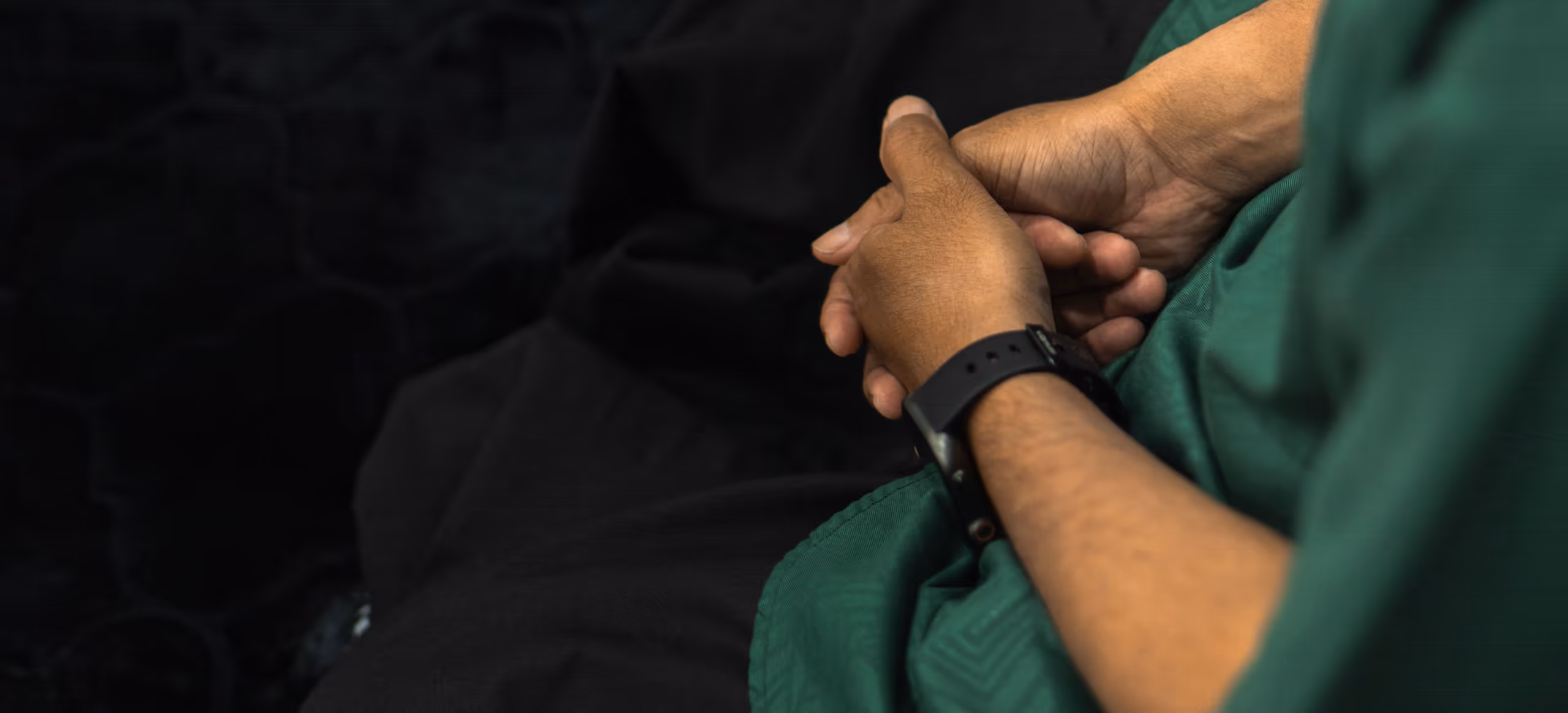 A pair of hands clasped in a lap over a green shawl
