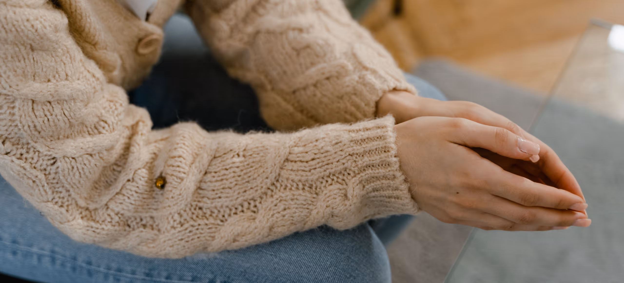 A person in a cream knit cardigan with their hands resting loosely in their lap