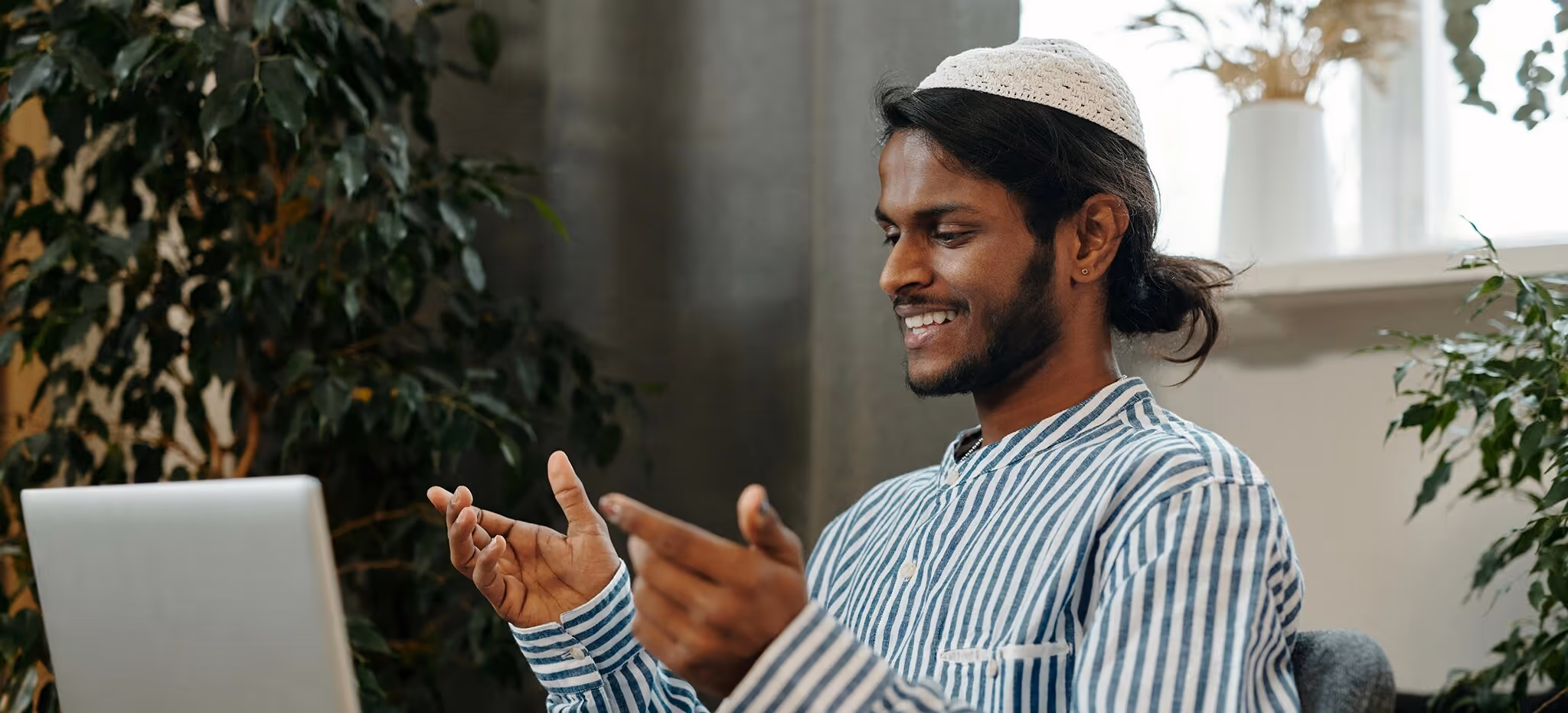 A smiling man in a kufi talking and gesturing during a video call at home