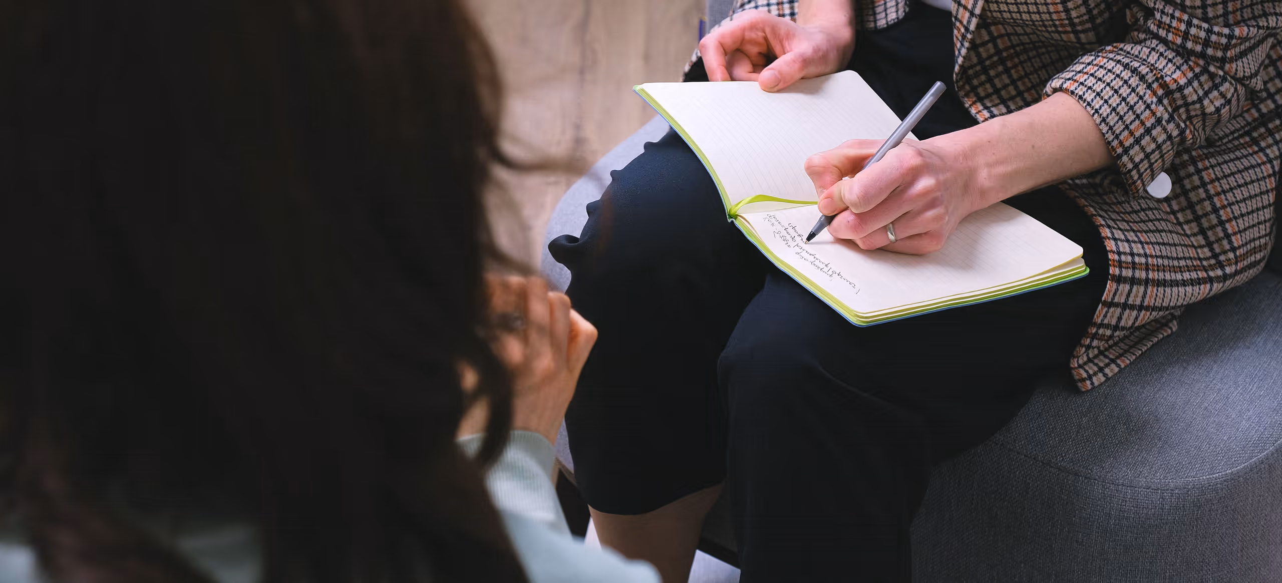 A therapist writing on a notepad across from a client seen from behind