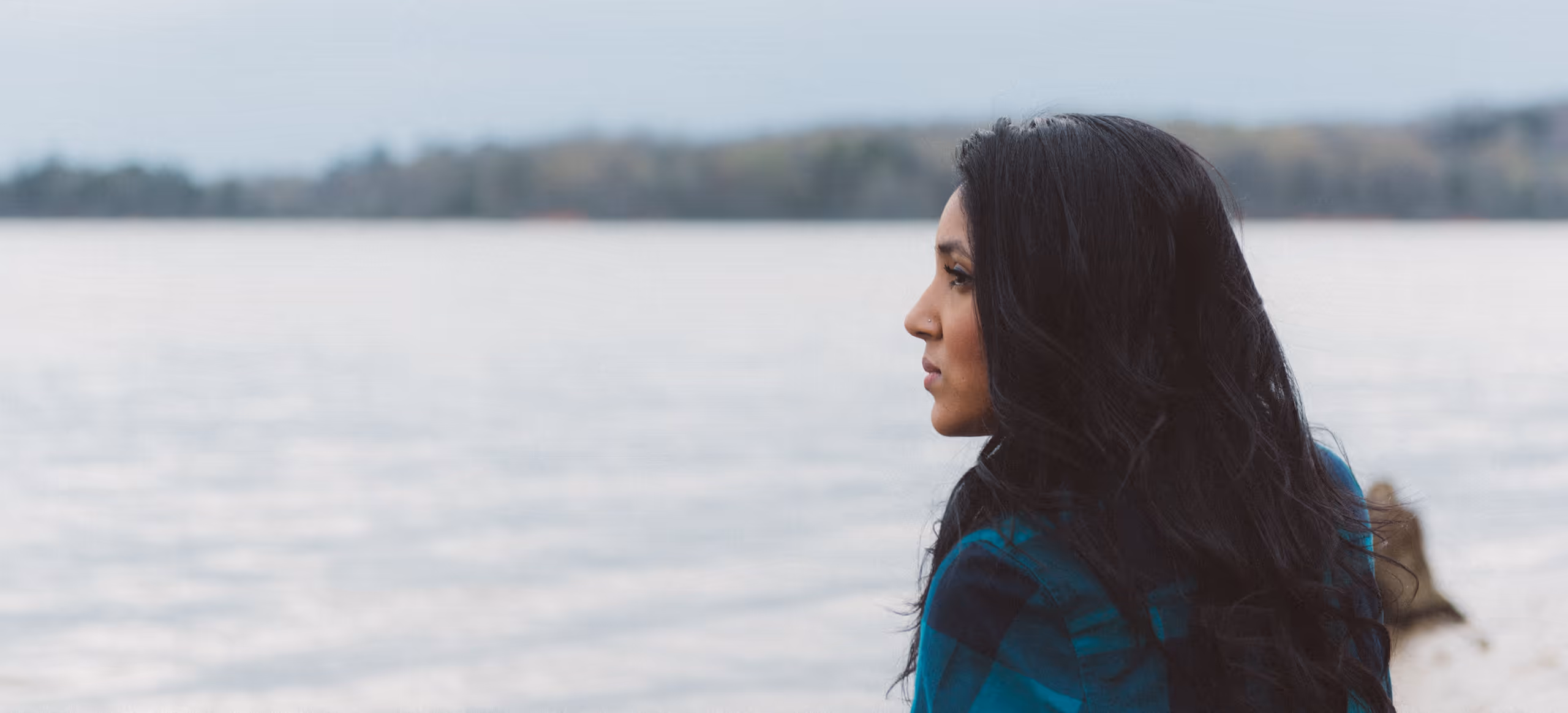 A woman in a plaid shirt seen in profile, looking out across a lake